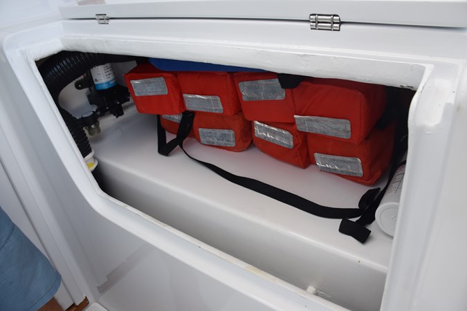 Starboard side beneath helm chair. Life preserver storage above fuel tank
